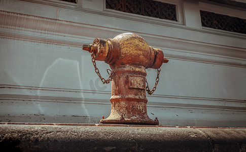 白色水泥墙前的人行道上有一个旧的红色消防栓，用于陆地灭火，水通过消防栓泵到火上的水箱。