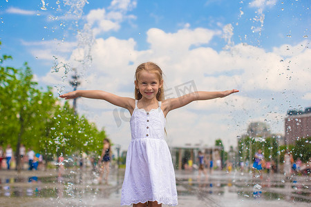 在炎热的阳光明媚的日子里，在开放的街道喷泉中行走的可爱小女孩