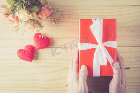 礼品盒白色蝴蝶结缎带手和心与木头上的花
