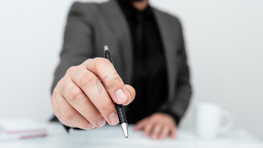 身穿灰色西装的男模特坐在白桌旁，用笔指着重要信息。