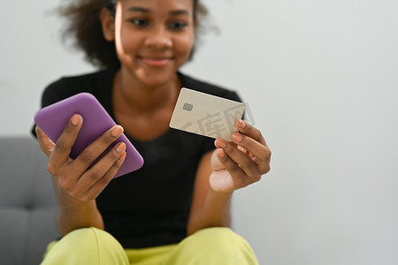 满意的年轻女性手持信用卡在手机上查看银行账户
