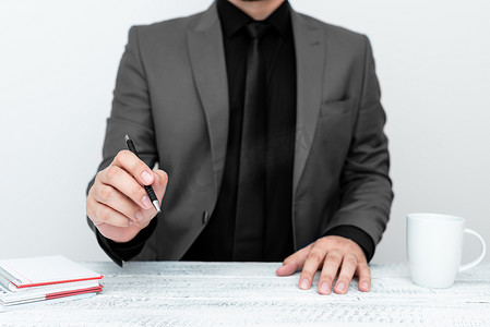 身穿灰色西装的男模特坐在白桌旁，用笔指着重要信息。