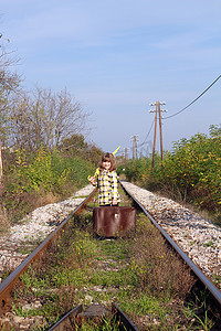 带着手提箱和雨伞站在铁路上的小女孩