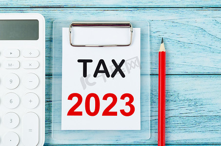 会计学摄影照片_剪贴板上的 Tax 2023 文本，木制背景上带有计算器。 