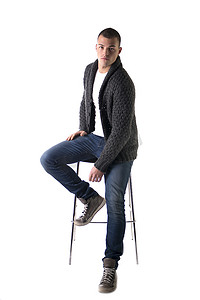 有魅力的年轻人坐在凳子上，穿着羊毛衫和牛仔裤