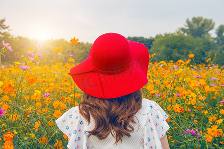 女人在花田里戴着一顶红色的帽子。