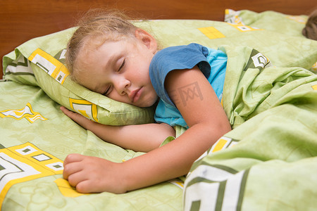 小女孩侧睡在床上，手放在枕头下，盖着毯子