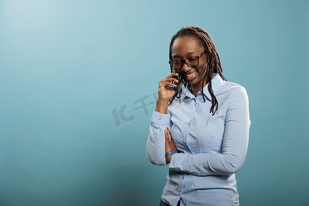 快乐快乐的年轻女子在蓝色背景下进行电话交谈时衷心微笑。