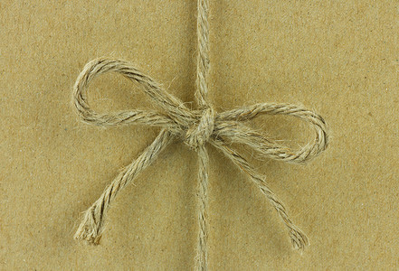 蝴蝶结绳子摄影照片_在棕色再生纸上系成蝴蝶结的绳子