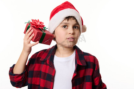 戴着圣诞帽的好奇小男孩，摇晃圣诞礼盒，猜测里面的礼物，在白色背景中突显