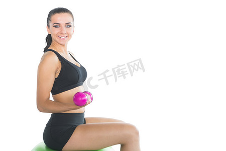 用粉色哑铃坐在健身球上的漂亮苗条女人