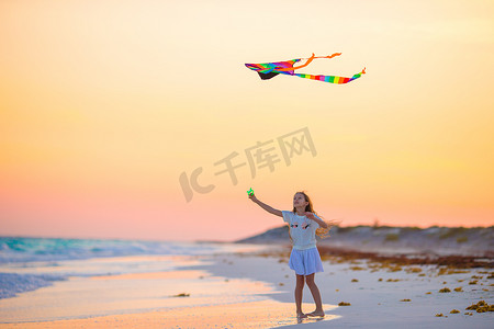 游戏娱乐摄影照片_日落时在热带海滩上放风筝的小女孩。