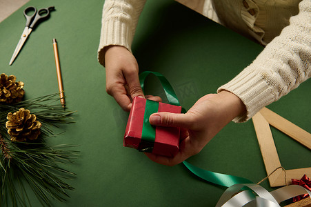 木板箱摄影照片_特写女人捆绑礼物，用红纸和绿胶带包裹。