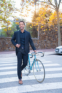 马路循环摄影照片_穿着西装骑着自行车过马路的时尚非洲裔美国商人。