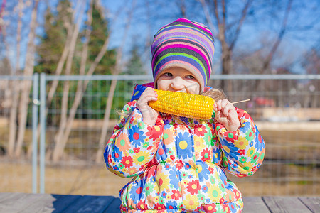 温暖的春日在公园里吃玉米的小可爱女孩