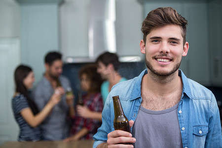 微笑的男人拿着啤酒瓶，而背景中的朋友
