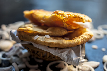 特写新鲜油炸的 bhatura 或 bhature 或 puri 以及黑色表面上的一些切洋葱圈。