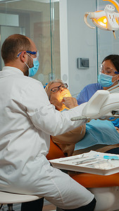老年牙齿摄影照片_牙医在诊所为老年女性患者治疗牙齿