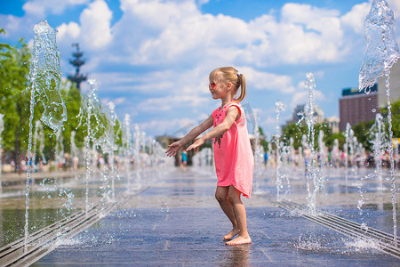清爽一夏天摄影照片_阳光明媚的炎热日子里，可爱的小女孩在街头喷泉里玩得开心