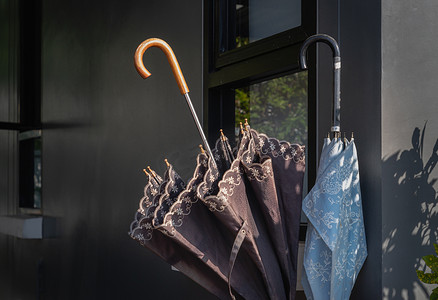 阳光照耀在房子外侧墙边的用木头做的雨伞储藏室里的棕色和蓝色雨伞上。