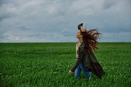 一个穿大衣的女人在多云的天气里站在田野里抵抗强风