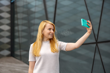 追随者摄影照片_年轻的金发女人在智能手机上为她的追随者自拍。