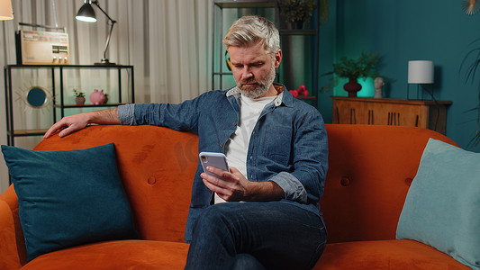中年老人坐在沙发上，使用智能手机在社交媒体应用程序上分享消息