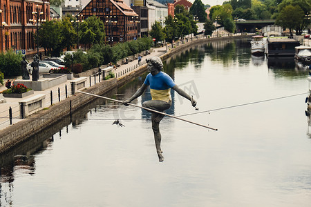 波兰比得哥什 - 2022 年 8 月，比得哥什的布尔达河男子穿越河流雕塑，一名男子在钢丝上保持平衡，旧粮仓建筑，库亚维-波美拉尼亚。