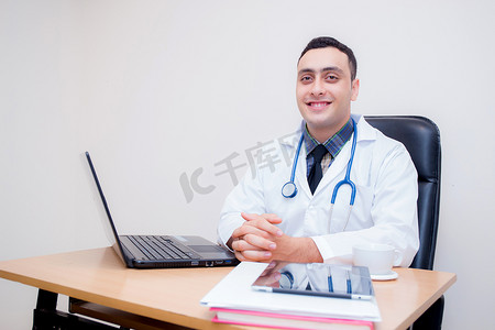 自信的男医生坐在办公桌前微笑，医学