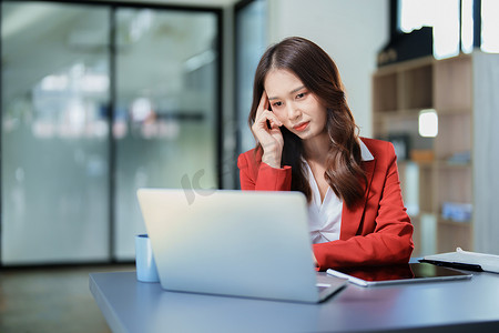 一张美丽的亚洲女员工的画像，她在使用办公桌上的电话和财务文件时表情紧张