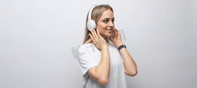 水平照片：一位身穿白色背心的年轻女性在白色背景下用无线耳机收听播客，有自由空间