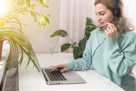 侧视头像微笑的混血女自由职业者戴着耳机，通过视频计算机通话与客户沟通。