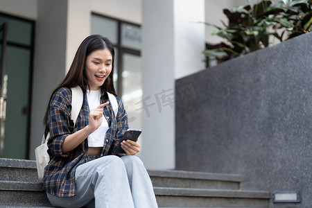 背光的人摄影照片_日落时，一名快乐的学生在街上用温暖的背光在街上行走和使用智能手机