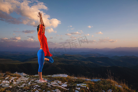 运动女性在山中阳光的夕阳下，在瑜伽中以树姿站立