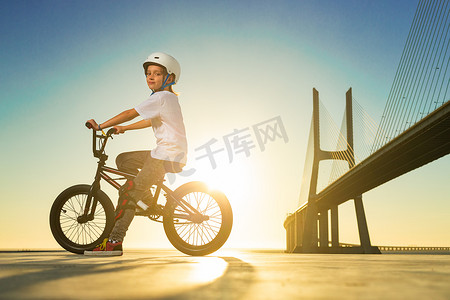 一轮太阳摄影照片_一名少年 BMX 赛车手在滑板公园的泵道上表演技巧。
