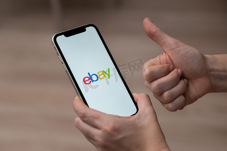 2022汇报摄影照片_2022 年 12 月 3 日，哈萨克斯坦阿拉木图：一位女士拿着带有 ebay 应用程序的智能手机并竖起大拇指。