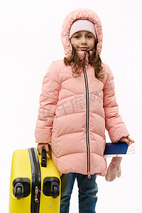 穿着粉色羽绒服、去寒假、在白色背景下拿着登机牌和手提箱的可爱女婴