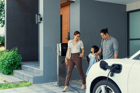 进步的年轻父母和女儿住在有电动汽车的家里。