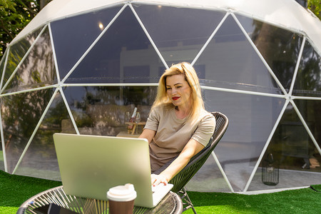 在笔记本电脑上工作的女人户外泡泡帐篷屋圆顶-自然旅行概念。