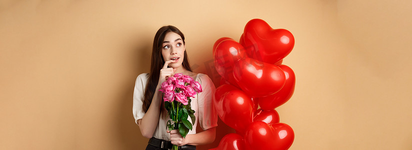 梦幻般的年轻女人手捧玫瑰花束，想着情人节的秘密仰慕者，看着左上角，咬着手指，站在红色浪漫气球旁