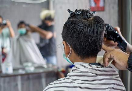 面罩摄影照片_戴着面罩的十几岁男孩正在理发店理发。