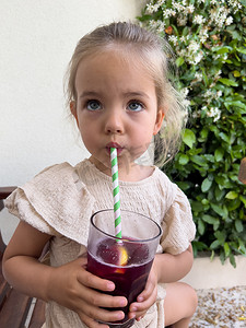 小女孩用手里拿着玻璃杯的吸管喝果汁