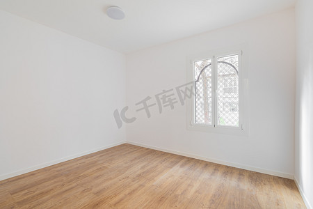 空荡荡的房间，铺有复合地板，新粉刷成白色的墙壁，窗户明亮。