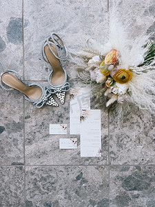 婚礼花束站在新娘鞋、邀请函和戒指旁边的瓷砖上