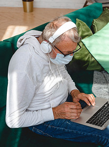 因冠状病毒而戴面罩的银发老人在家中使用笔记本电脑 — 现代科技和退休人员