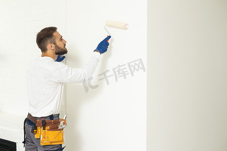 粉刷滚筒摄影照片_画家用油漆滚筒粉刷房屋墙壁。