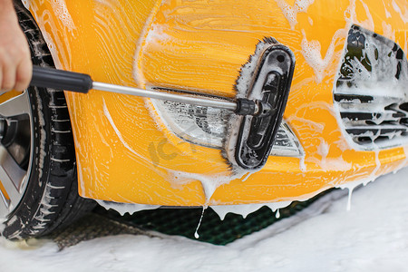 黄色汽车的前保险杠和灯在自助洗车中清洗，用白色洗发水刷洗。