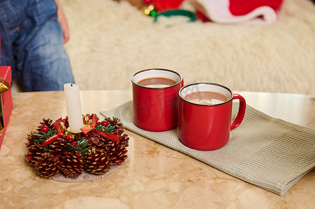 绿色餐巾纸上放着热可可饮料的红杯，旁边是大理石桌上装饰性的圣诞蜡烛。