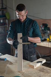 木匠车间摄影照片_木匠在车间工作时测量木板。