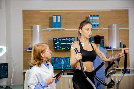 女运动员在步进器上做体力，并在她身上握住电极，医生手持平板电脑